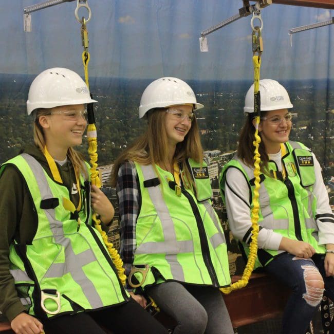 Three middle school girls pose in front of a skyscraper background