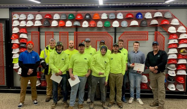 Group of Carpentry I graduates stand in front of the WMCI hard hat wall with their instructor - Clark Causely