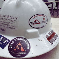 A hardhat with several different stickers from a variety of construction companies in West Michigan