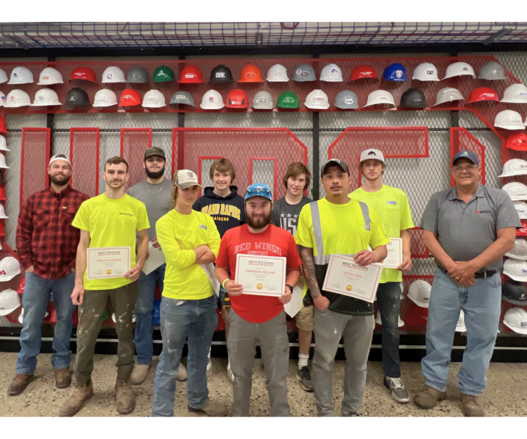 Group of carpentry graduates in front of the WMCI hard hat wall